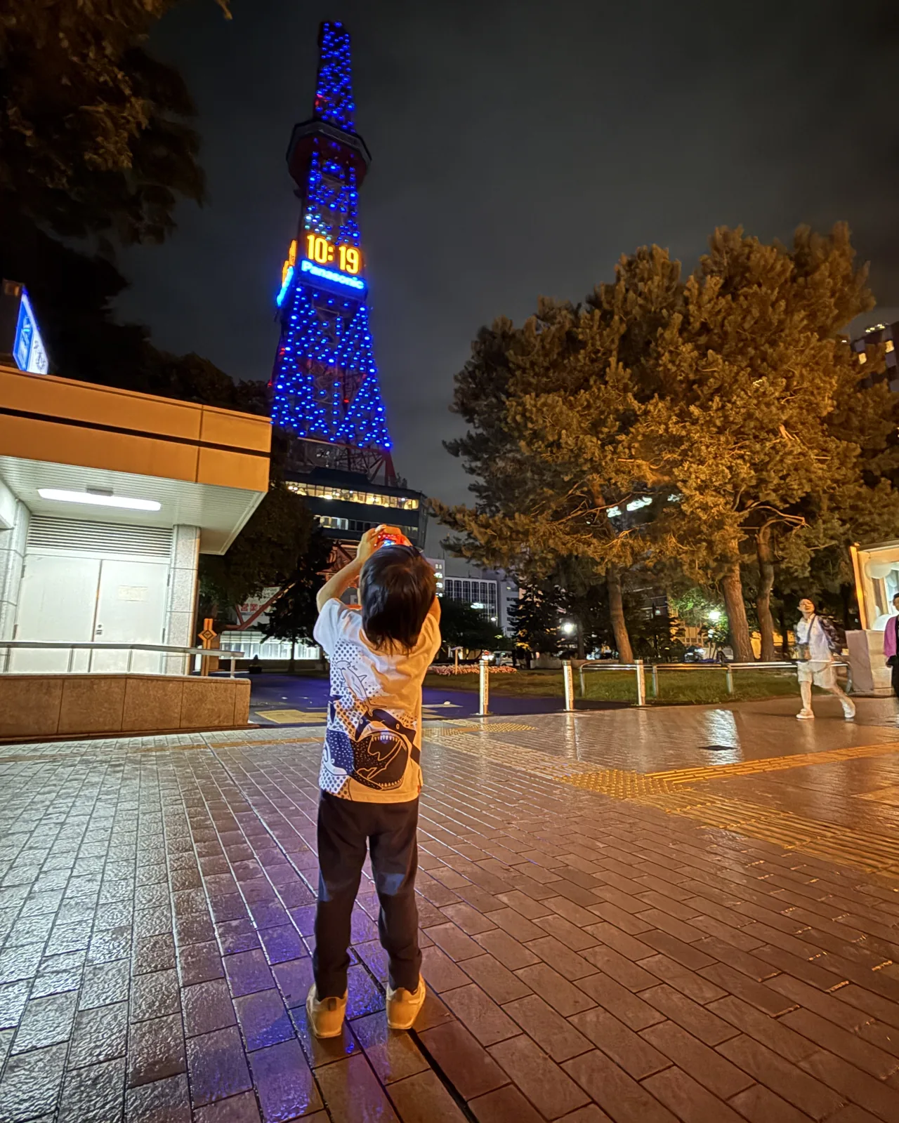 夜晚的札幌電視塔,一個小孩背對鏡頭舉起相機在拍它